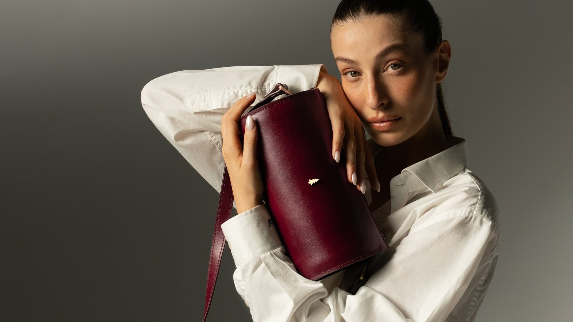 ARAS PINE — burgundy vanity bag with brass pine emblem on white shirt