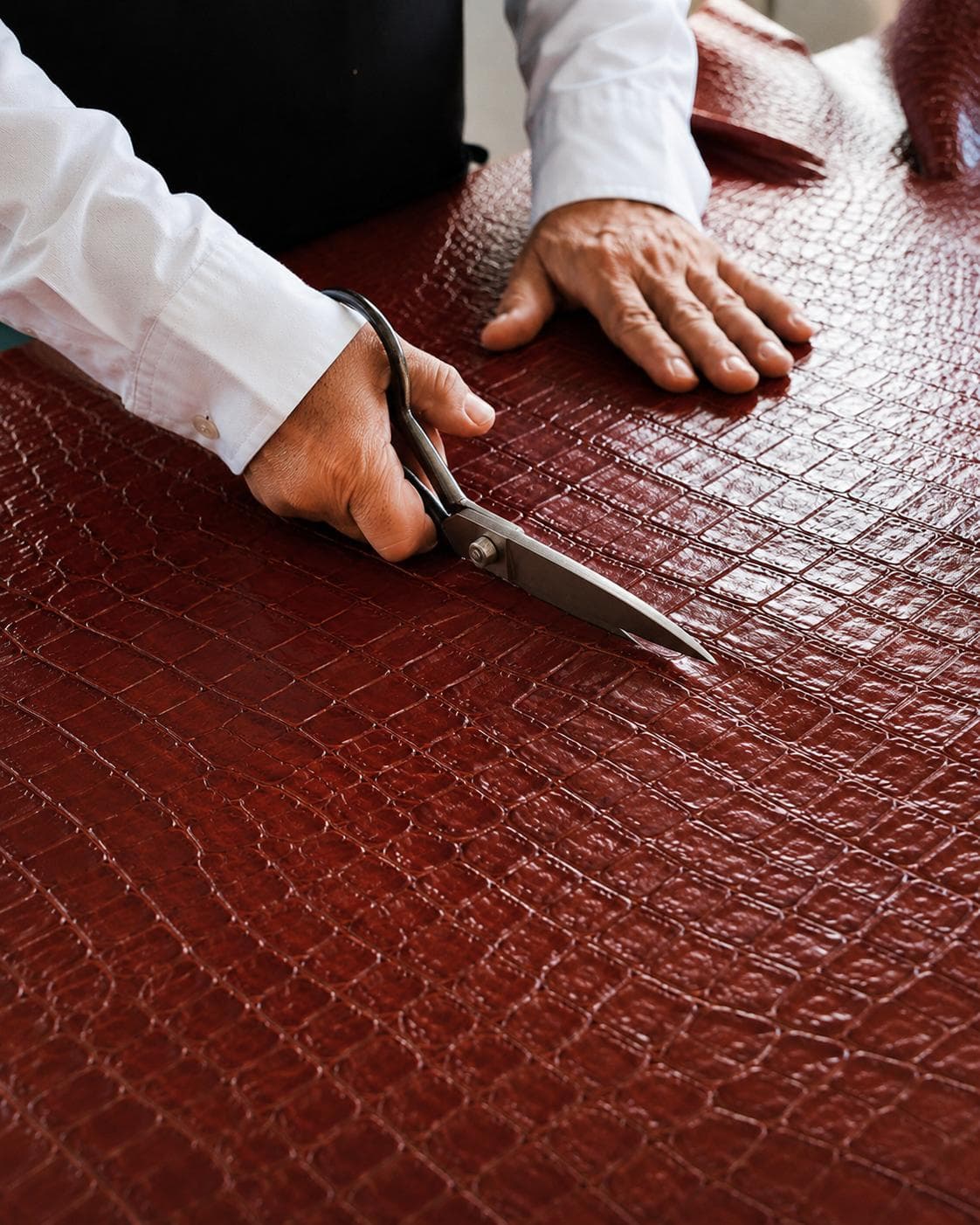 Craftsperson hand-cutting burgundy crocodile-embossed leather