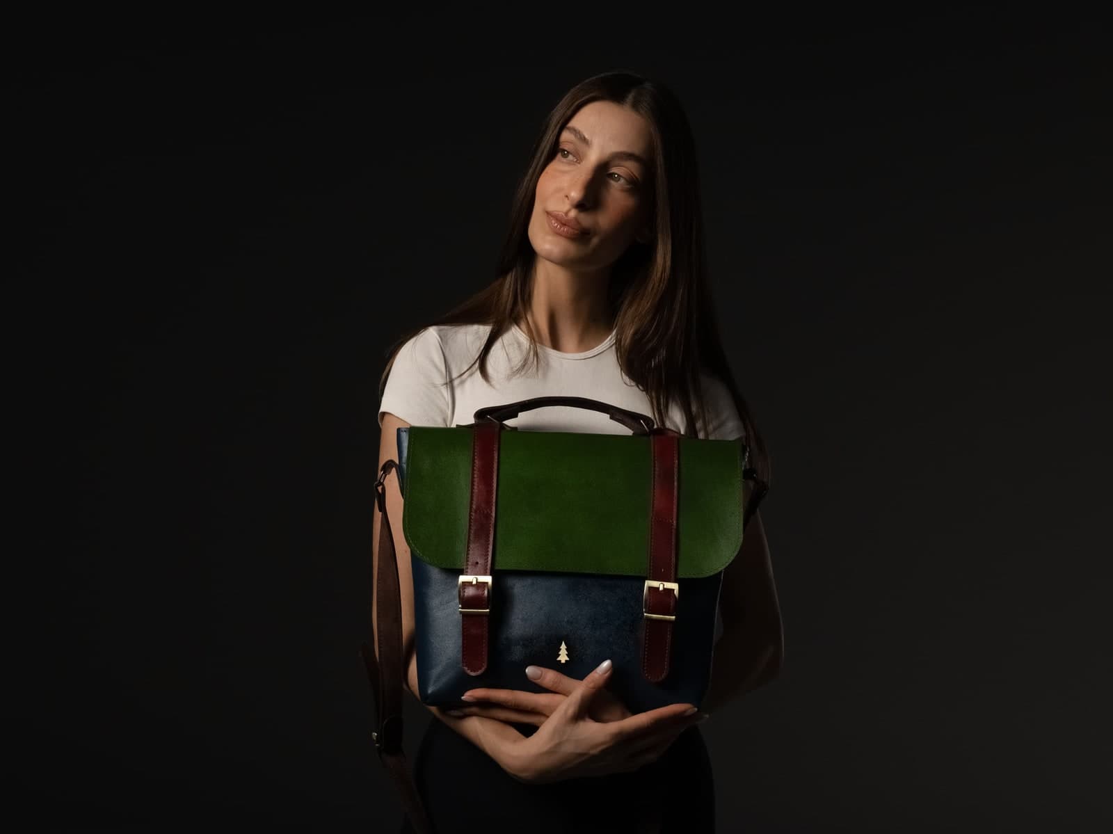 ARAS PINE Liore Messenger — green flap, navy body — White tee under a hard side-spot; the tri-tone panel reads whole against a black backdrop. Suede, calfskin, brass.