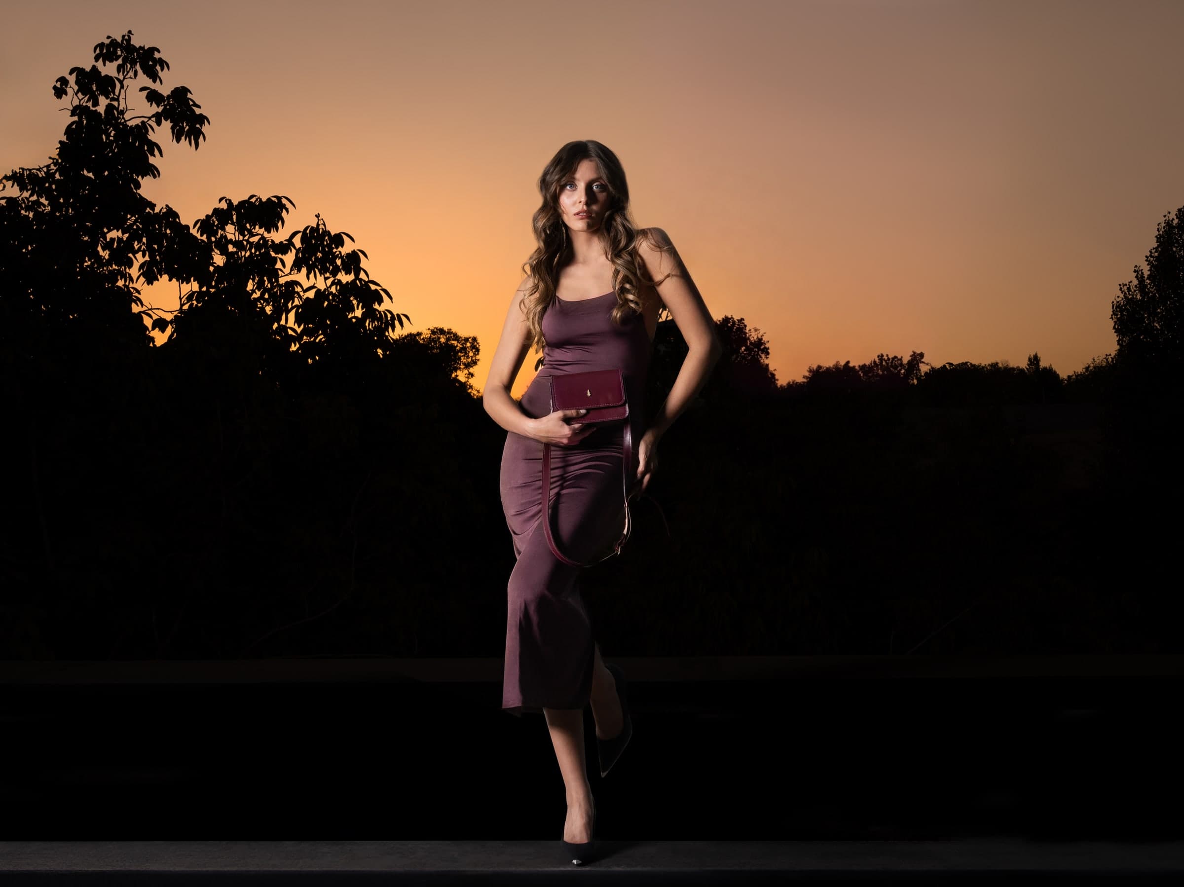 ARAS PINE Devon Crossbody — burgundy — Silhouetted at the tree line as the day closes; the burgundy piece held at the hip. A crossbody cut for the moment the working day gives way to the evening after.