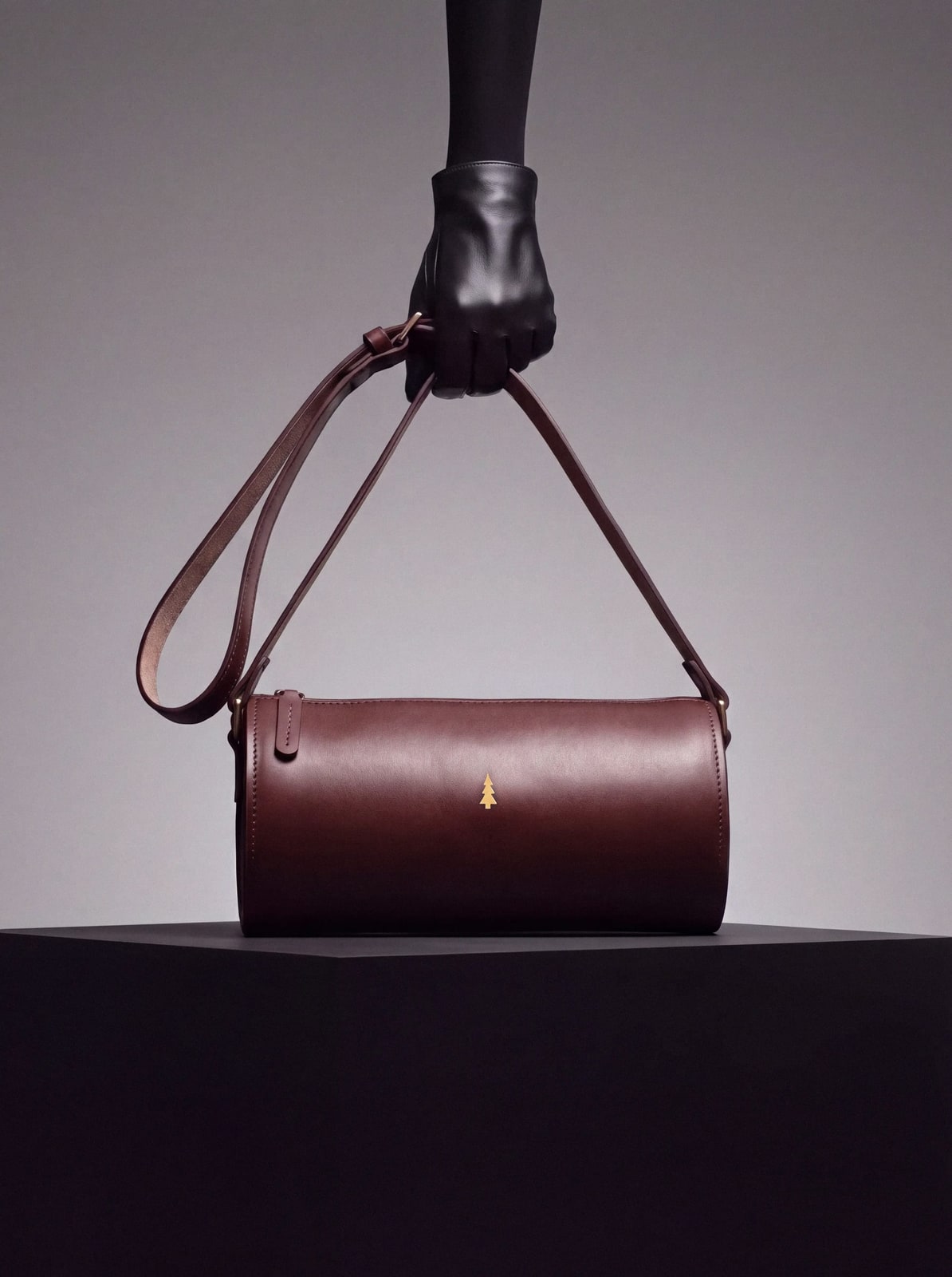 ARAS PINE Crossbody — burgundy barrel, held by a gloved hand against a soft grey backdrop — leather crossbody bag, handmade in Türkiye