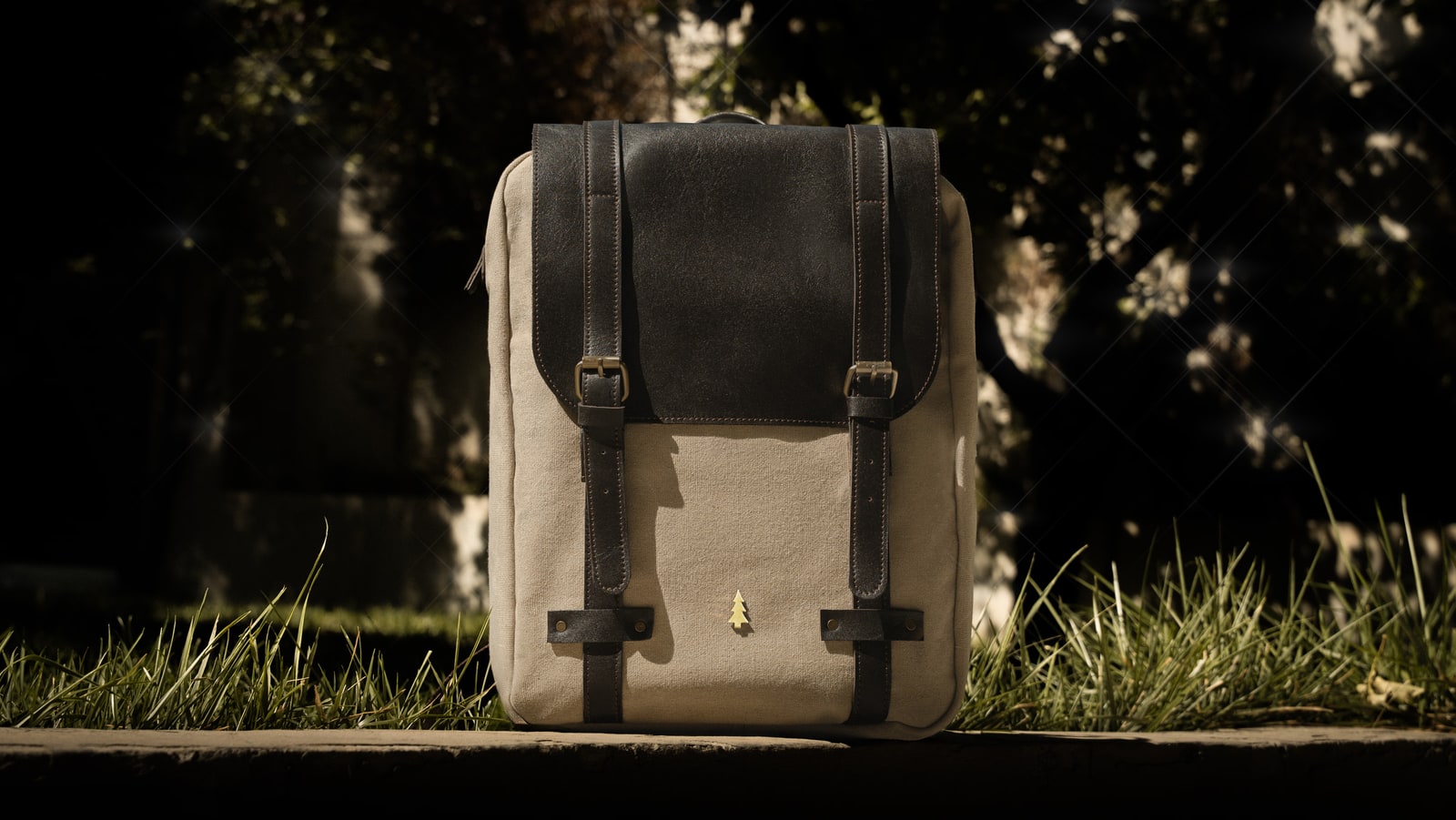ARAS PINE Ferrando Backpack — cream canvas & chocolate leather, on a stone ledge at dusk with a shaft of sunlight cutting the garden behind — leather backpack, handmade in Türkiye