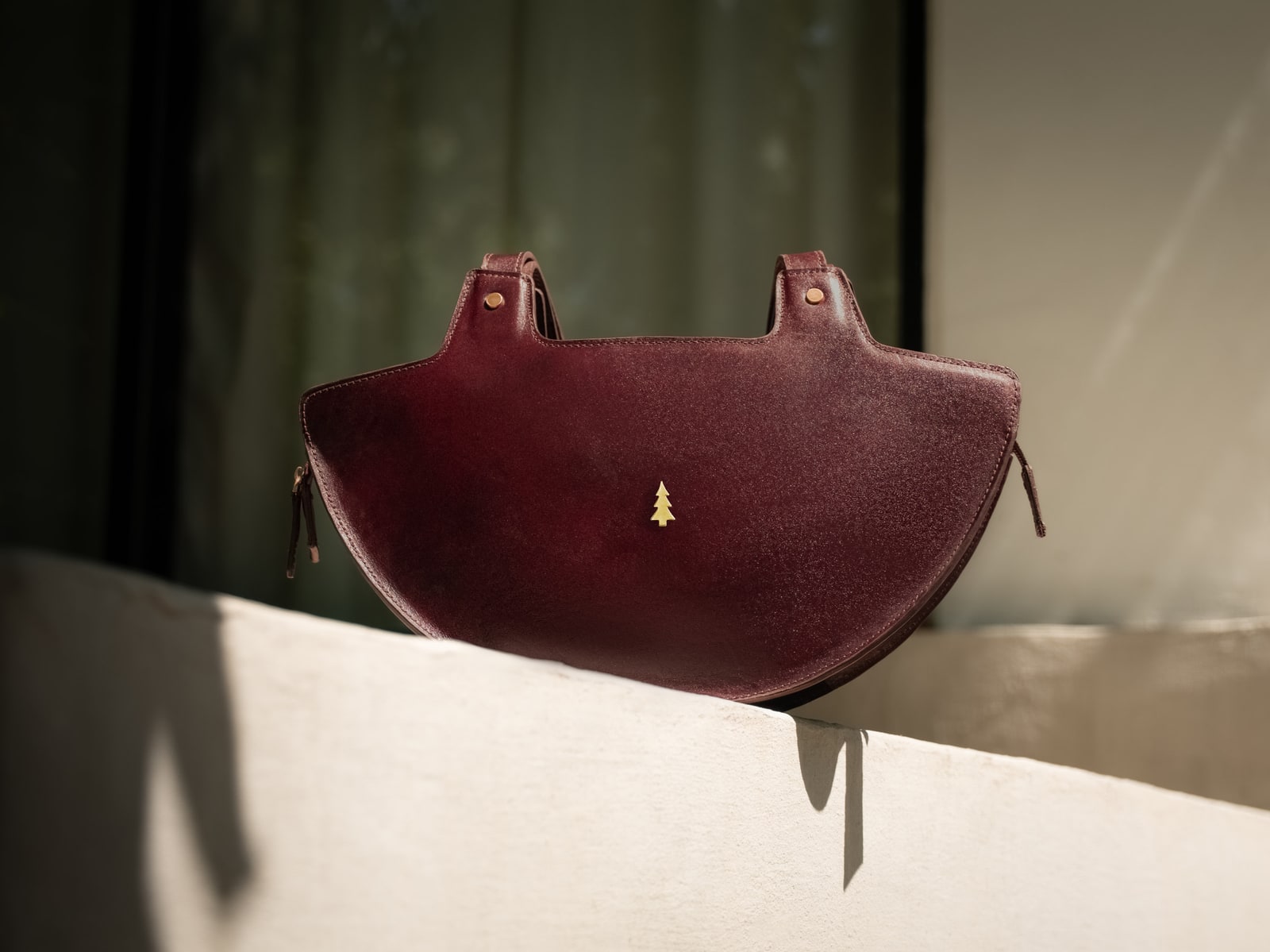 ARAS PINE Luna Handbag — burgundy half-moon silhouette on a pale stone ledge in raking sunlight — leather handbag, handmade in Türkiye
