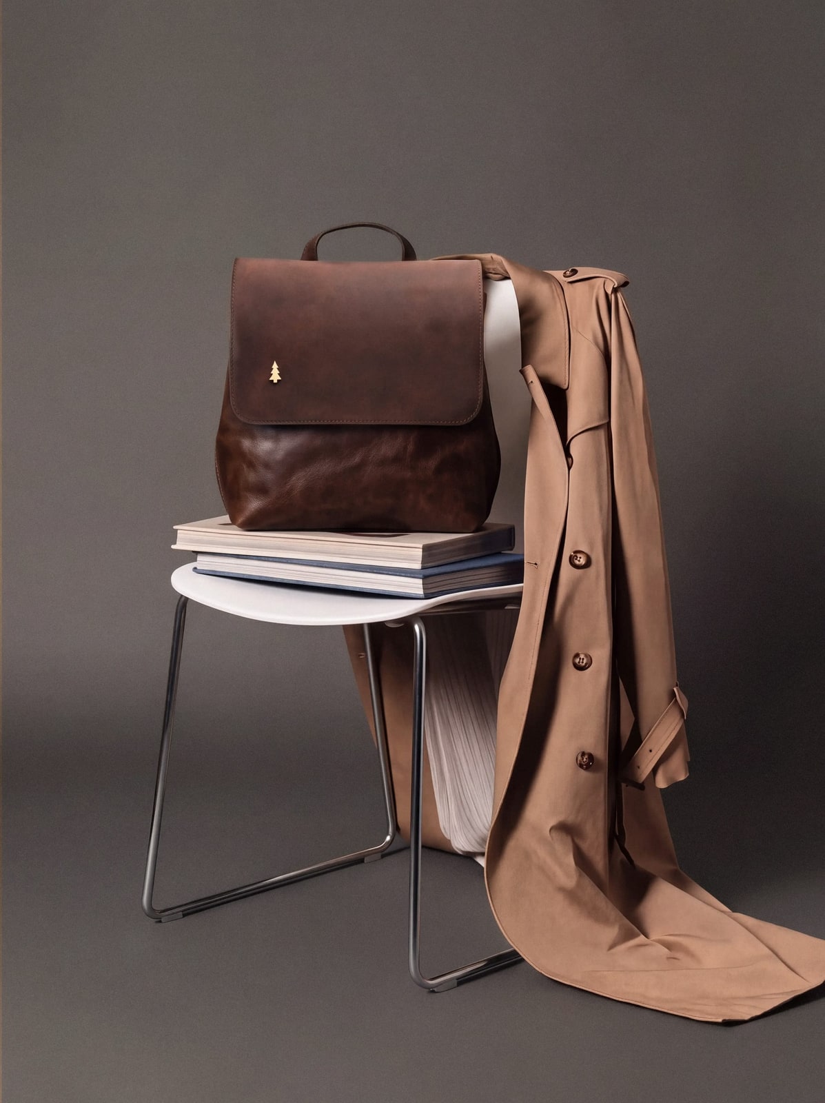 ARAS PINE Marcel Backpack — dark chocolate, on a chair with a trench coat draped over — leather backpack, handmade in Türkiye